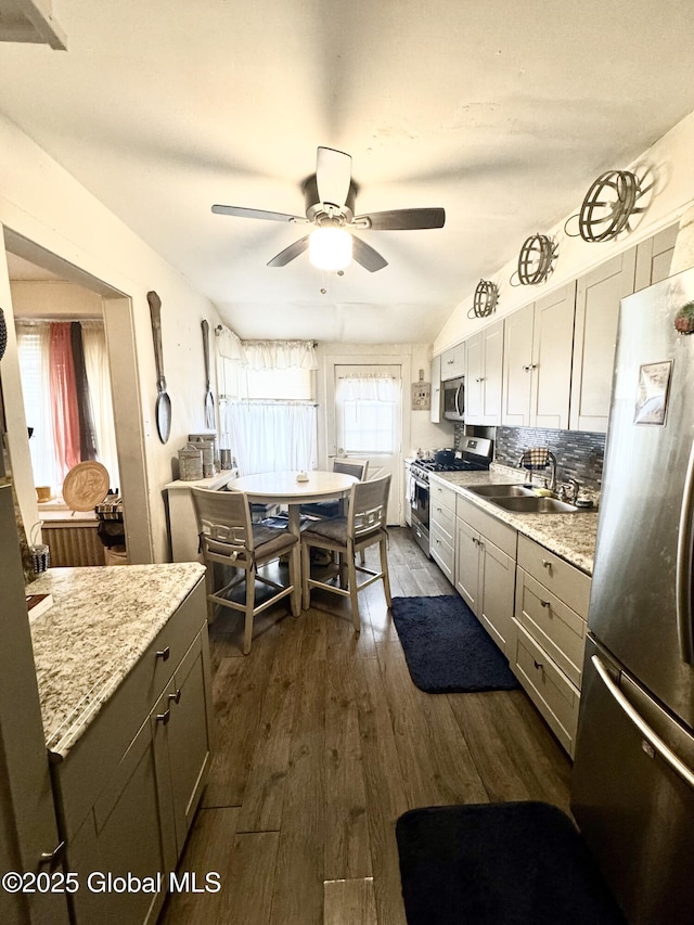 kitchen with a sink, backsplash, ceiling fan, appliances with stainless steel finishes, and dark wood-style flooring