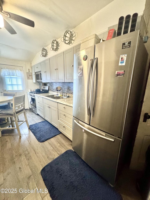 kitchen with a sink, tasteful backsplash, stainless steel appliances, light wood-style floors, and light countertops