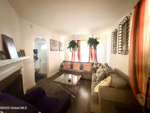 living room featuring arched walkways, a fireplace, baseboards, and wood finished floors