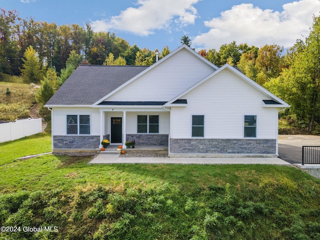 view of front of property featuring a front yard, fence, stone siding, and a shingled roof