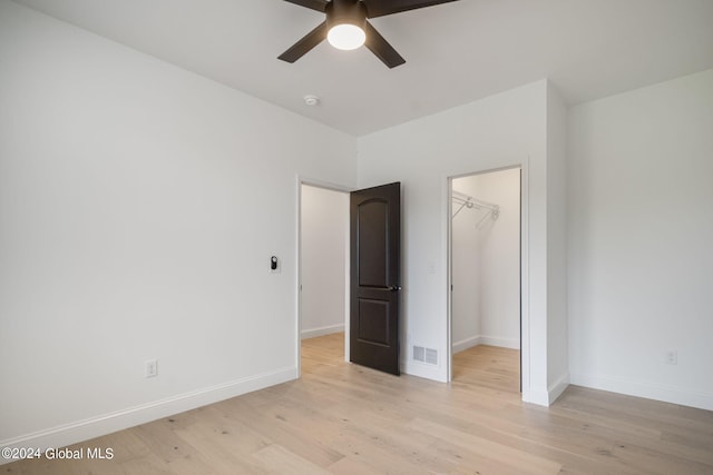 unfurnished bedroom featuring visible vents, a walk in closet, a closet, light wood finished floors, and baseboards