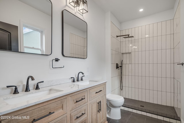 bathroom featuring tile patterned flooring, tiled shower, toilet, and a sink