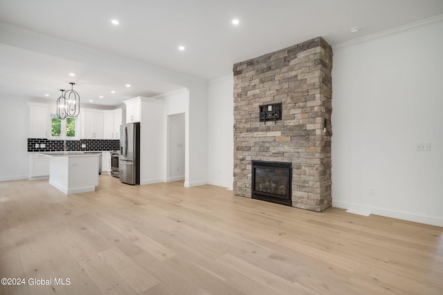 unfurnished living room featuring a large fireplace, baseboards, a chandelier, ornamental molding, and light wood-style floors