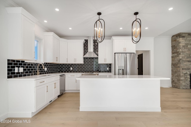 kitchen with a kitchen island, appliances with stainless steel finishes, light wood-style floors, wall chimney exhaust hood, and a sink