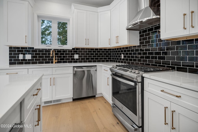 kitchen featuring light wood-type flooring, a sink, appliances with stainless steel finishes, wall chimney range hood, and decorative backsplash