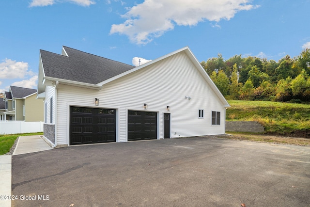 view of side of home with aphalt driveway, fence, and a shingled roof