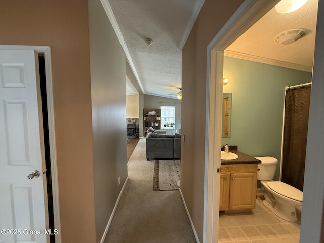 hall featuring light carpet, lofted ceiling, ornamental molding, a textured ceiling, and baseboards