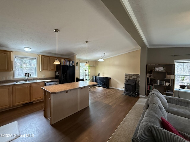 kitchen featuring light brown cabinets, a wood stove, a sink, open floor plan, and black fridge