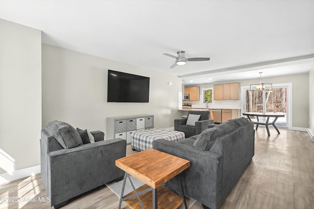 living room featuring baseboards, light wood-style flooring, and ceiling fan with notable chandelier