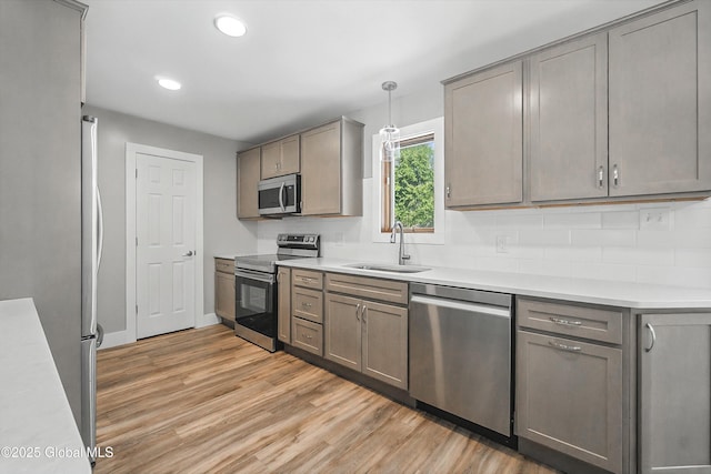 kitchen featuring gray cabinetry, light wood-style flooring, a sink, appliances with stainless steel finishes, and light countertops