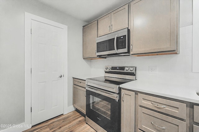 kitchen with wood finished floors, gray cabinets, light countertops, appliances with stainless steel finishes, and tasteful backsplash