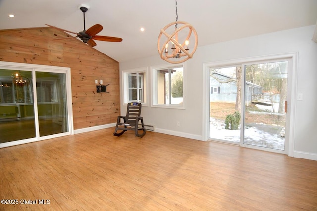 interior space with wooden walls, wood finished floors, baseboards, vaulted ceiling, and ceiling fan with notable chandelier