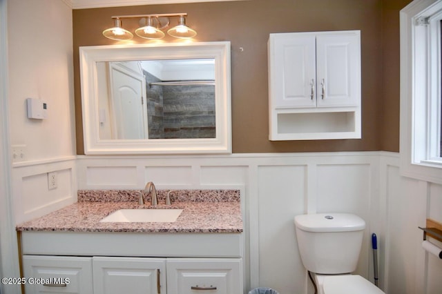 bathroom featuring vanity, a decorative wall, toilet, and a wainscoted wall