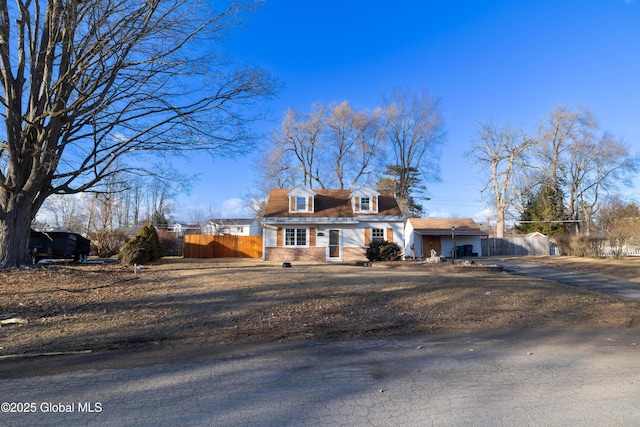 cape cod house featuring brick siding and fence