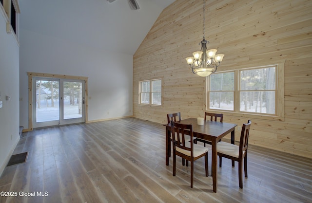 dining space featuring visible vents, high vaulted ceiling, wooden walls, and wood finished floors