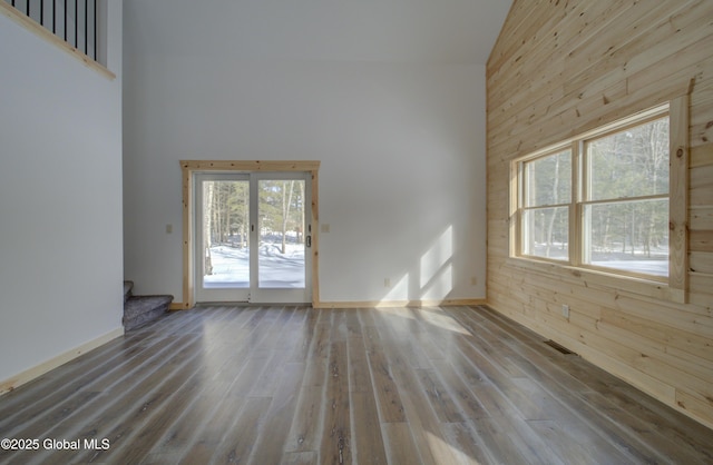 spare room featuring wooden walls, stairway, a towering ceiling, and wood finished floors