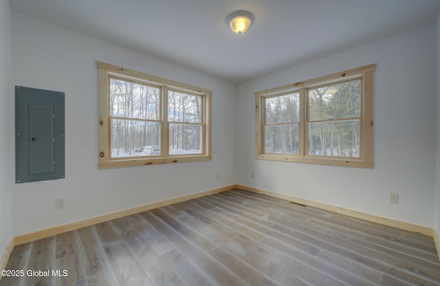 spare room with electric panel, wood finished floors, and baseboards