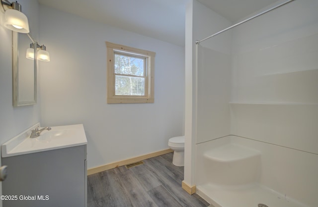 bathroom featuring baseboards, toilet, wood finished floors, vanity, and a shower