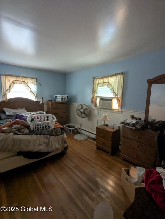 bedroom featuring a baseboard heating unit, multiple windows, wood finished floors, and cooling unit