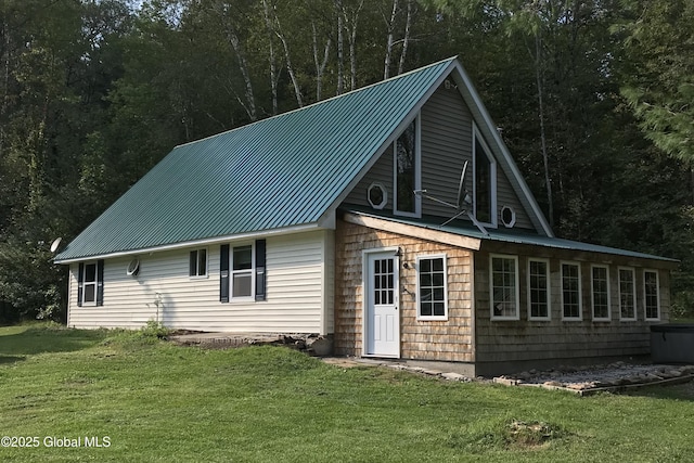 rear view of property featuring a yard, a wooded view, and metal roof