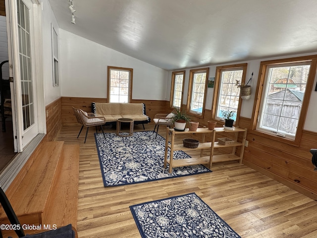 living room with vaulted ceiling, light wood finished floors, wood walls, and wainscoting