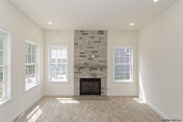 unfurnished living room with baseboards, carpet flooring, a stone fireplace, and visible vents