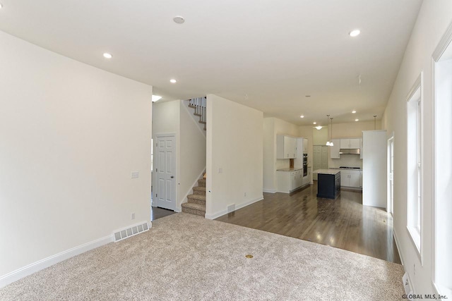 unfurnished living room with visible vents, recessed lighting, stairway, and dark carpet