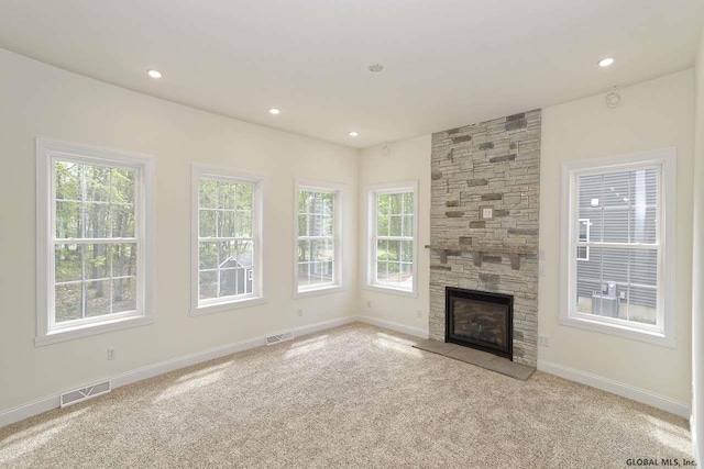 unfurnished living room with a stone fireplace, carpet, and visible vents