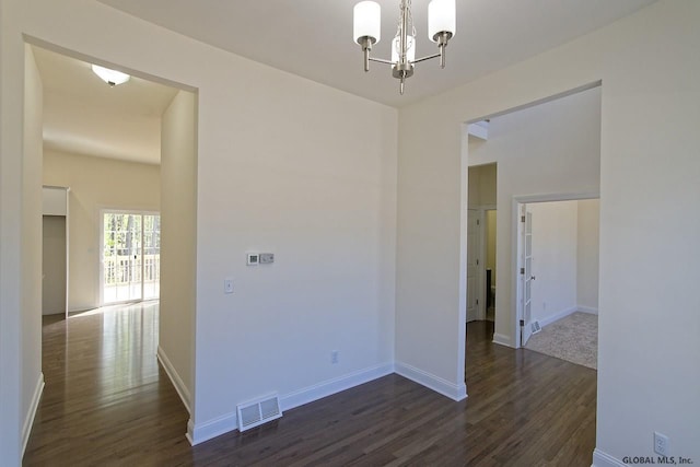 unfurnished room featuring a notable chandelier, visible vents, baseboards, and dark wood-style flooring