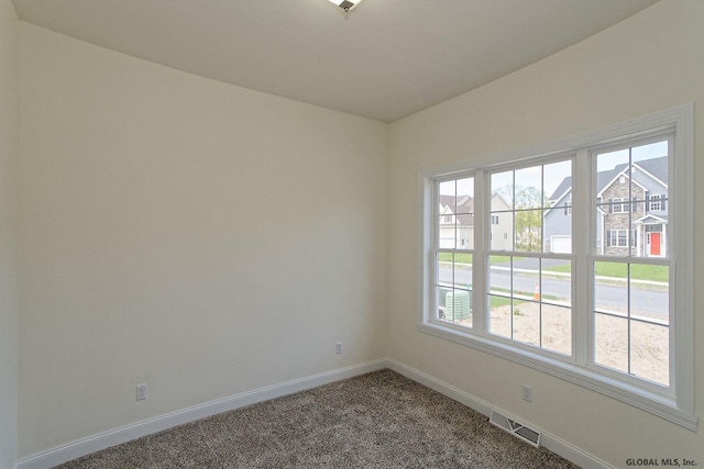 carpeted empty room with baseboards, visible vents, and a residential view