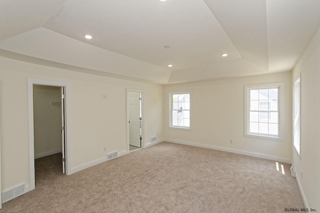 spare room with visible vents, light colored carpet, a raised ceiling, and baseboards