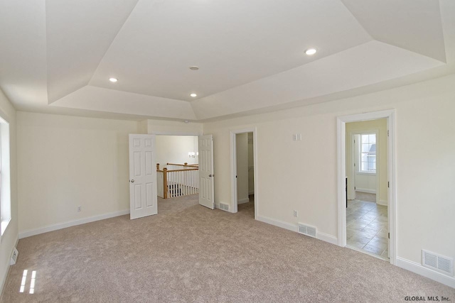 unfurnished bedroom featuring a raised ceiling, recessed lighting, visible vents, and light carpet