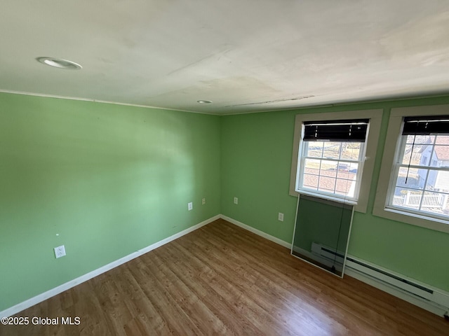 empty room featuring a baseboard heating unit, wood finished floors, and baseboards