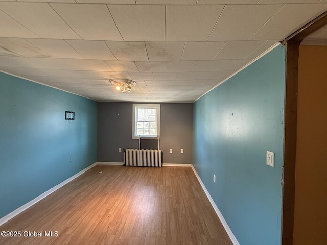 unfurnished room with radiator, wood finished floors, and baseboards