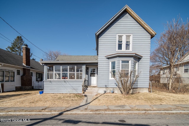 traditional home with entry steps, roof with shingles, and a sunroom