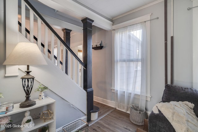 stairway featuring baseboards, wood finished floors, crown molding, and ornate columns