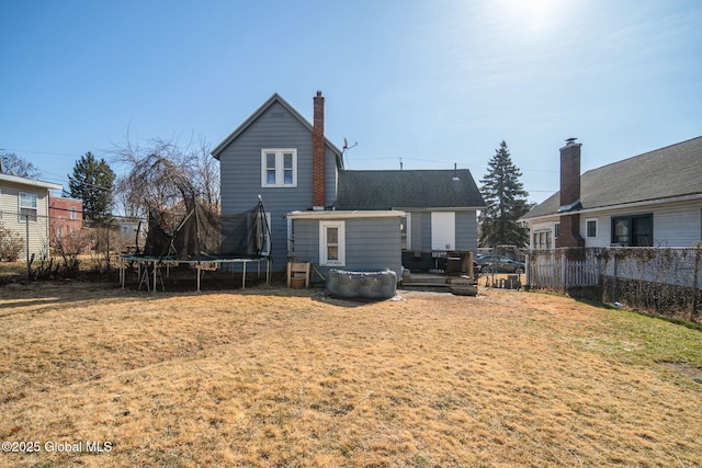 back of house featuring a yard, a chimney, a trampoline, and fence