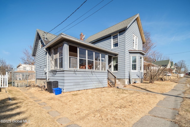 view of front of house featuring fence, roof with shingles, a chimney, and a sunroom