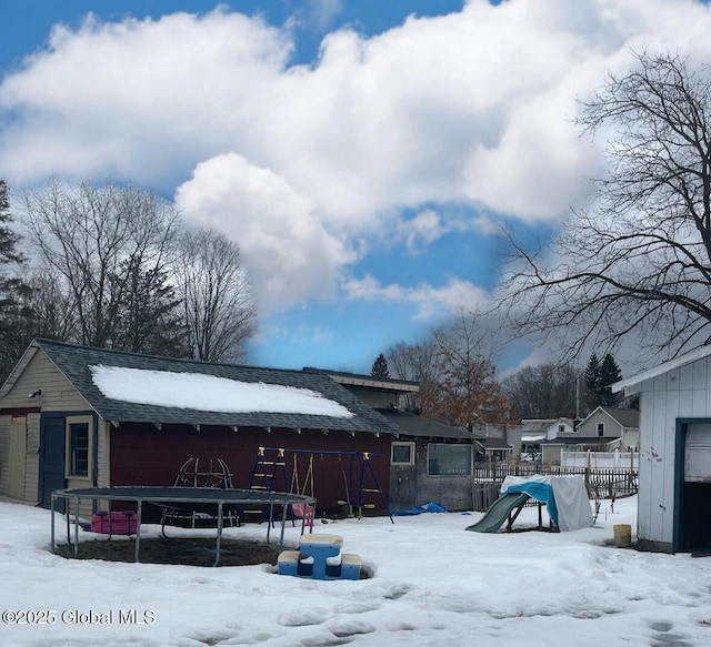 snow covered house featuring a playground, a trampoline, and fence