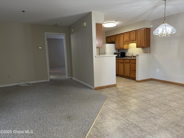 kitchen with brown cabinetry, freestanding refrigerator, baseboards, and decorative light fixtures