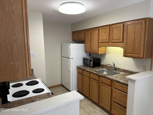 kitchen featuring brown cabinetry, freestanding refrigerator, a sink, cooktop, and stainless steel microwave