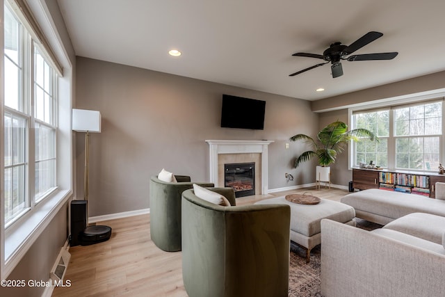 living area featuring a glass covered fireplace, light wood-type flooring, baseboards, ceiling fan, and recessed lighting