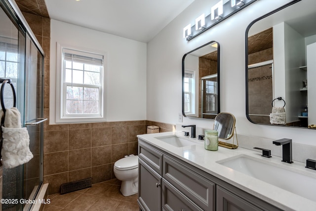 full bathroom featuring a sink, a stall shower, tile walls, and visible vents