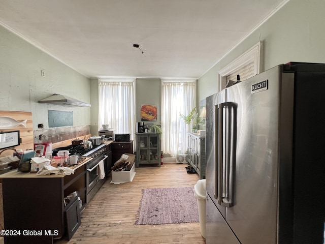 kitchen with light wood-type flooring, high end fridge, under cabinet range hood, dark cabinetry, and crown molding