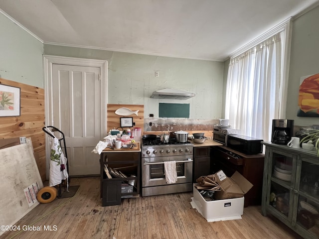 kitchen featuring under cabinet range hood, ornamental molding, stainless steel stove, and hardwood / wood-style floors