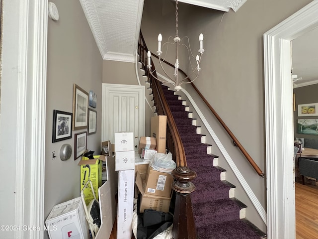 stairway featuring a notable chandelier, wood finished floors, and ornamental molding