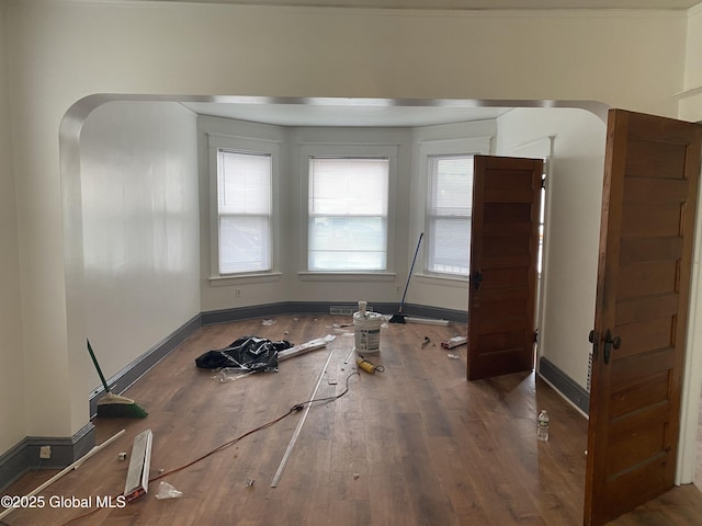 unfurnished dining area featuring wood finished floors, baseboards, and arched walkways