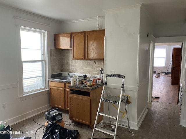 kitchen featuring tasteful backsplash, dark countertops, crown molding, brown cabinets, and a sink