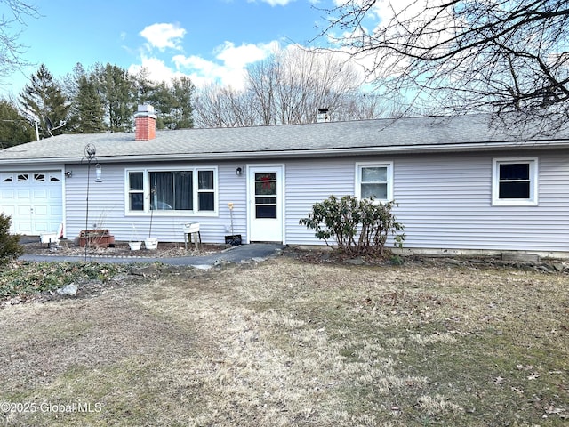 back of house with a garage, roof with shingles, and a chimney