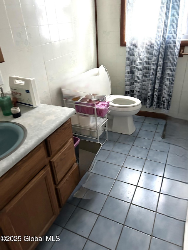 half bathroom with tile patterned flooring, tile walls, toilet, and vanity